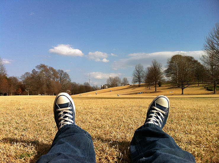 Legs in Converse shoes lying on the grass; photo by Ilham Rahmansyah, Unsplash.