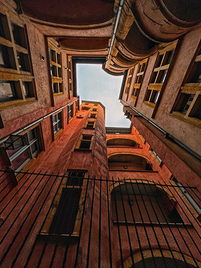 View of the tall building in Lyon, France, from the bottom of the inside courtyard, in the city famous for secret passageways called traboules; photo by Marian Muraru, Unsplash.