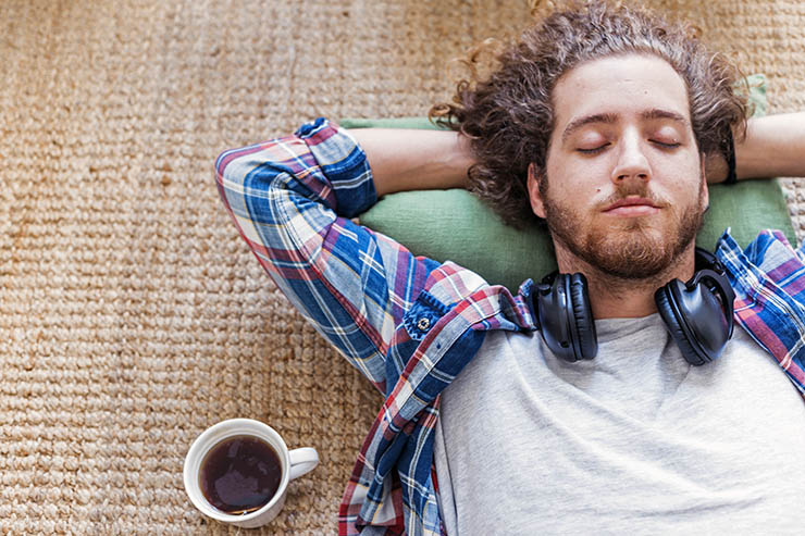 Man relaxing while taking a break on the floor, with a cup of tea; photo by Freepik.