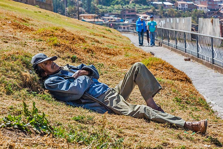 During siesta, an older man lying down on the grass by the walking path in Cusco, Peru; photo by Diego Delso.