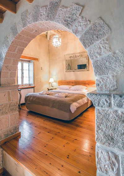 Double bed in the suite of Arstistas Hotel, Aristi, as seen through an arched stone door frame, in Zagori, Epirus, Greece; photo by Booking.com.