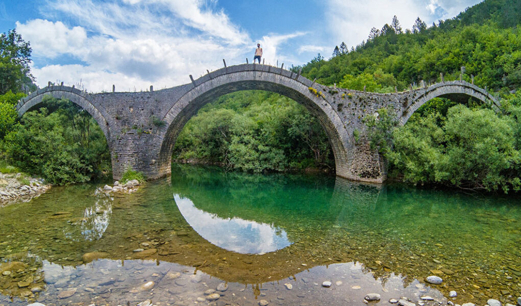 Travel blogger Ivan Kralj standing on a three-arch Plakidas Bridge in Zagori, Greece; photo by Nikos Samartzis.