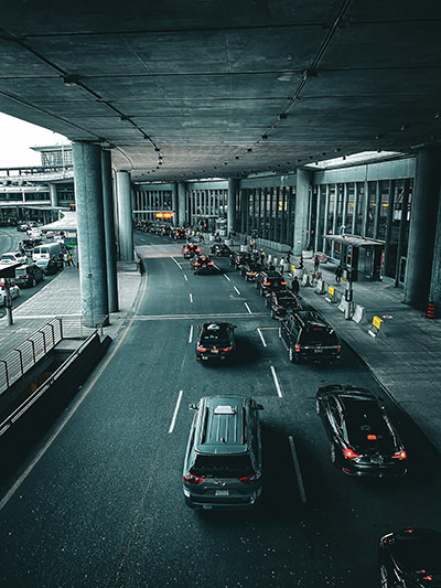 Cars and taxis waiting in front of the airport terminal building; photo by Jason Grant, Unsplash.
