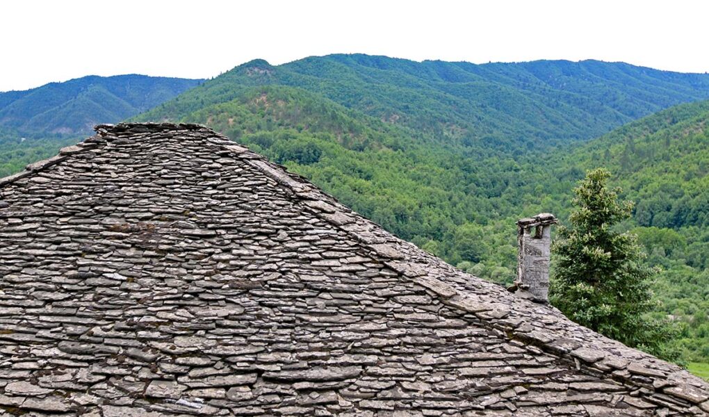 Slate roofing of a stone house in Kipoi, one of the Zagorochoria or Zagori villages in northwestern Greece, juxtaposed with green mountainous landscape; photo by Ivan Kralj.