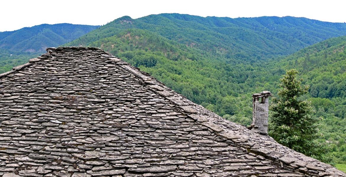 Slate roofing of a stone house in Kipoi, one of the Zagorochoria or Zagori villages in northwestern Greece, juxtaposed with green mountainous landscape; photo by Ivan Kralj.