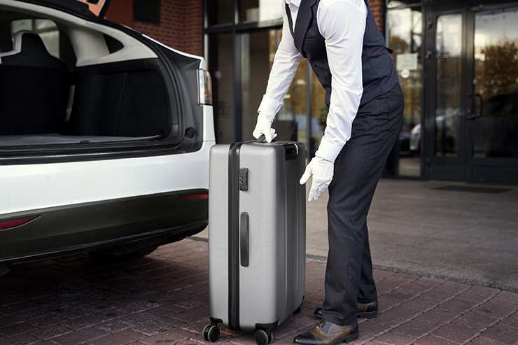 Valet personnel putting a suitcase in a car; image by Freepik.