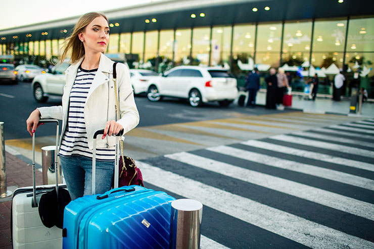 Young woman with suitcases at the zebra crossing in front of the airport building; photo by V. Ivash, Freepik.