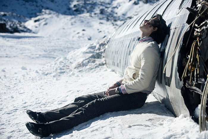 Scene from the Netflix movie "Society of the Snow" showing a survivor resting in the snow, leaning on the wreckage of the plane that crashed in the Andes in 1972.