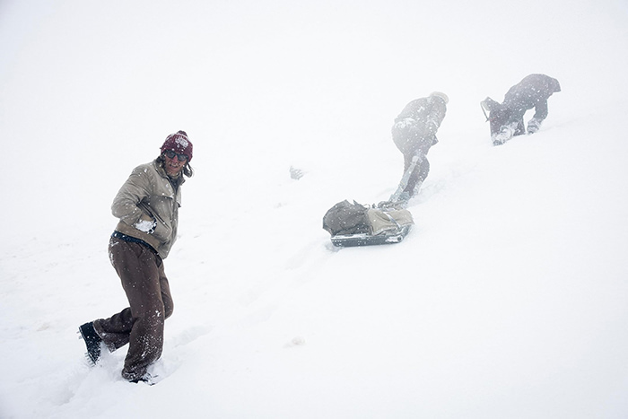 Scene from the Netflix movie "Society of the Snow" showing survivors trekking through the snow-covered Andes Mountain, with an improvised sled made from a suitcase.