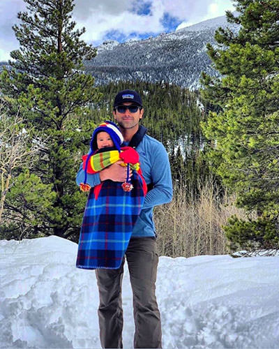 In the winter landscape of a national park forest, Eric Castillo holds his baby Journey in his hands, the first child that would visit all 63 national parks in the USA before turning three.