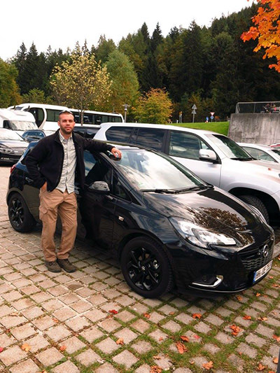 Travel blogger Joren Byers standing next to a rental car in Germany, on a trip where the GPS navigation led him to the wrong hotel of the same name in another city.