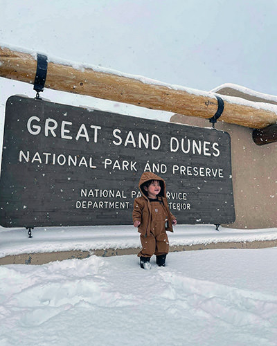Toddler Journey Castillo standing in the snow at the Great Sand Dunes, one of the 63 national parks she would visit before turning 3.