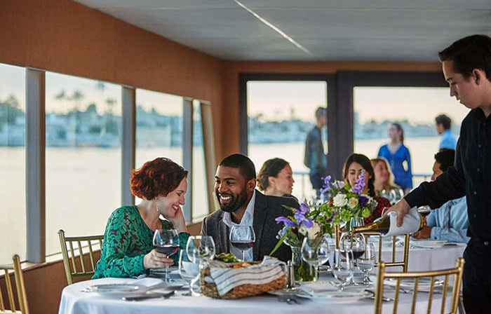 Couple enjoying dinner while waiter pours wine on Los Angeles dinner city cruise, California, GetYourGuide; one of Valentine food gift ideas.
