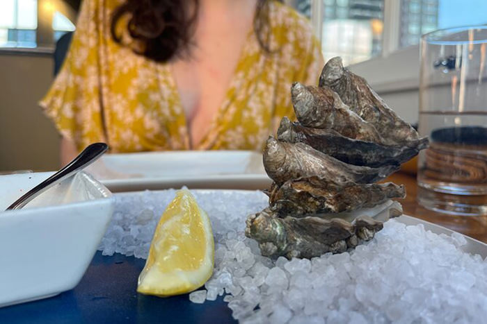Oysters served on ice and with lemon in a restaurant, with woman in the background, part of Seattle seafood brunch tour, Viator, one of Valentine food gift ideas.