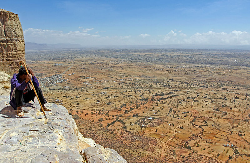 Pilgrim sitting on the edge of the cliff in Gheralta Mountain, Ethiopia, enjoying the panoramic views; photo by Ivan Kralj.