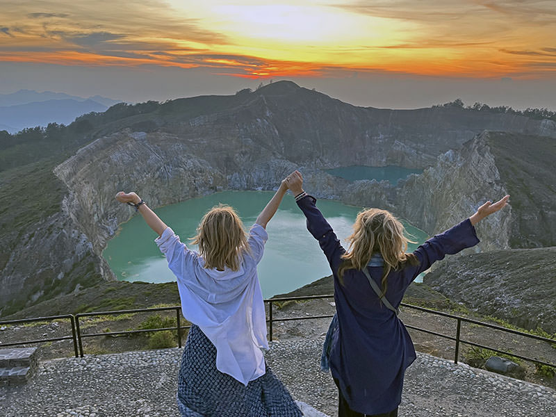 Rosa and Shannon Coggins raising hands in front of the crater lakes on Java, Indonesia, during their slow travel journey to Australia, without planes.