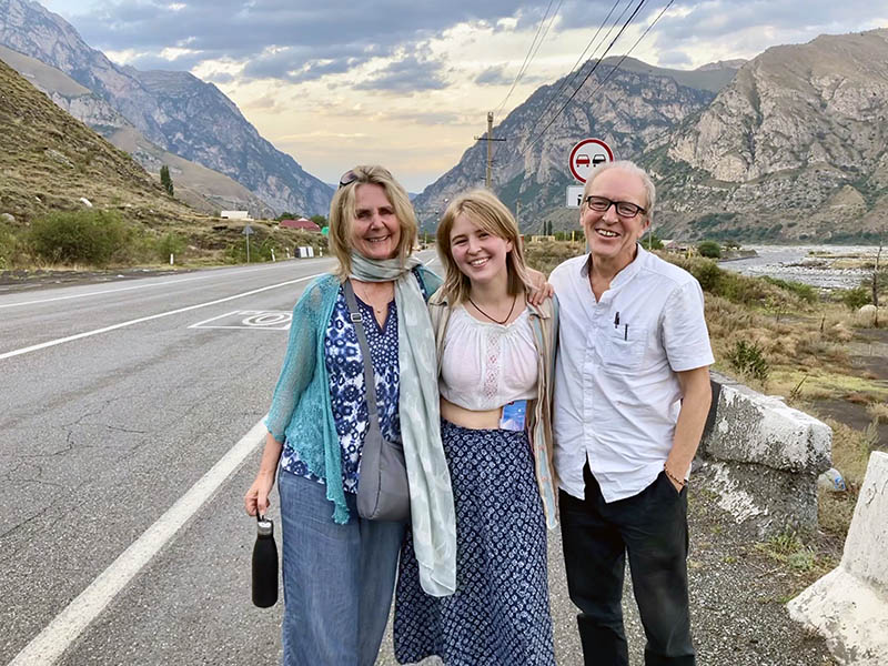 Shannon Coggins, Rosa, and Theo Simon, a slow travel family from the UK, standing by the road, on their way to Australia, without planes.