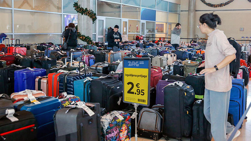 People browsing through a great quantity of suitcases displayed with a yellow sign "Lost Luggage €2.95", and logo of Zagreb Airport; a photoshopped image for the purpose of lost luggage scam on fake Facebook pages.