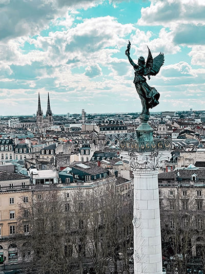 A statue of an angel with Bordeaux cityline in the background; photo by Tiphaine Sauveur, Unsplash.