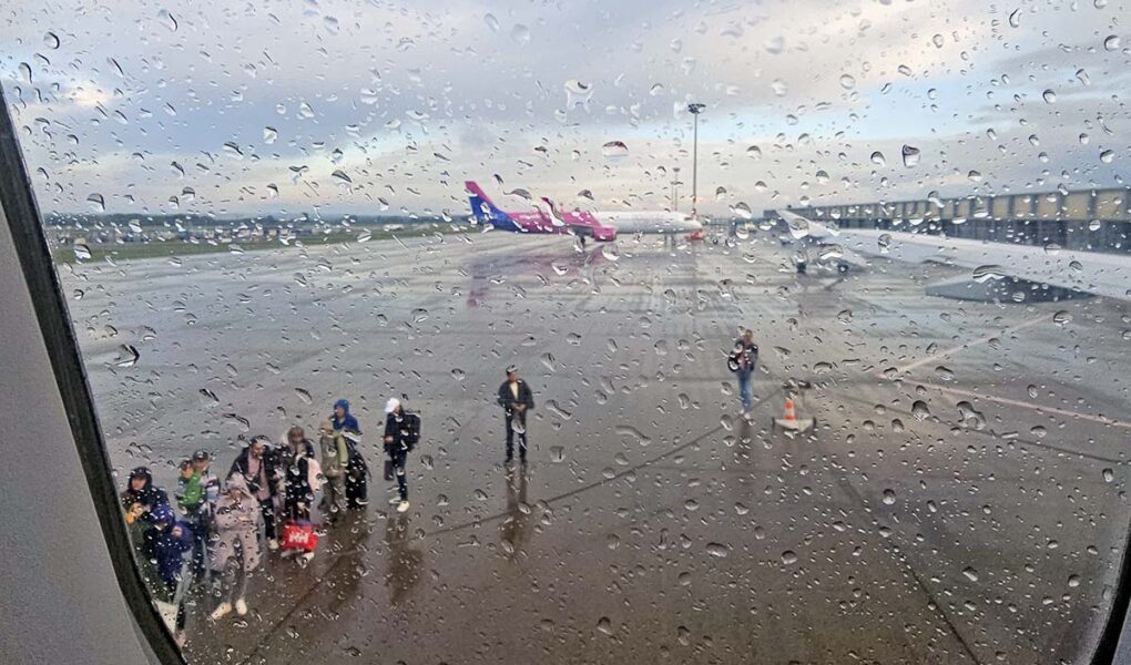 On a rainy day, passengers waiting at Budapest Airport tarmac to board the Wizzair plane, as seen through a wet plane window; photo by Ivan Kralj.