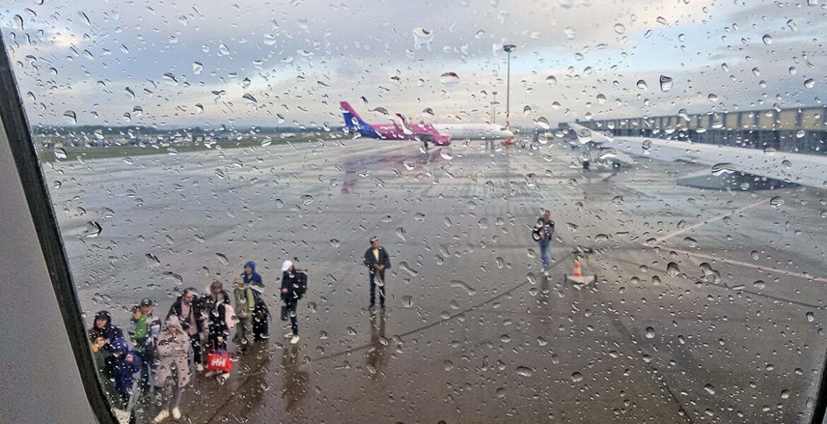 On a rainy day, passengers waiting at Budapest Airport tarmac to board the Wizzair plane, as seen through a wet plane window; photo by Ivan Kralj.