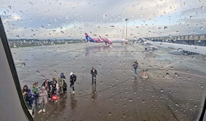 On a rainy day, passengers waiting at Budapest Airport tarmac to board the Wizzair plane, as seen through a wet plane window; photo by Ivan Kralj.