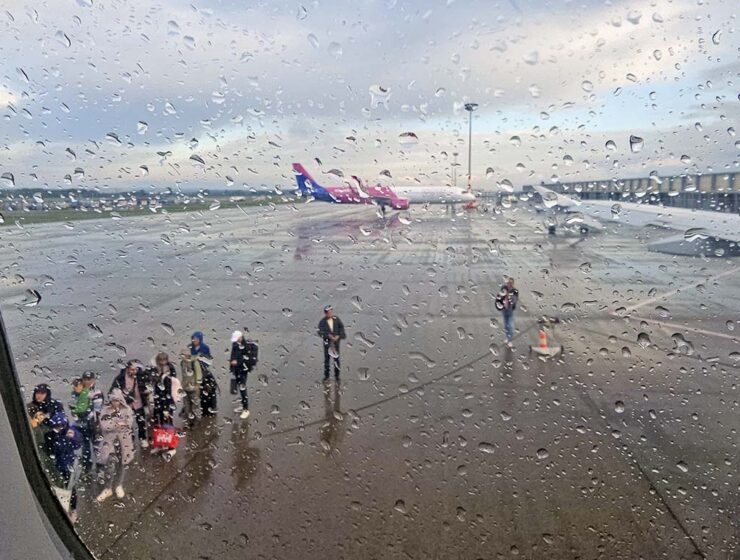 On a rainy day, passengers waiting at Budapest Airport tarmac to board the Wizzair plane, as seen through a wet plane window; photo by Ivan Kralj.