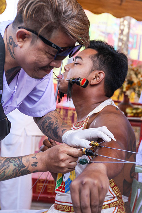 A piercer piercing the arm skin of a man, a ma song spirit medium at Jor Soo Goong Naka Shrine, during Jay or Phuket Vegetarian Festival, also known as Thailand's self-mutilation festival; photo by Ivan Kralj.