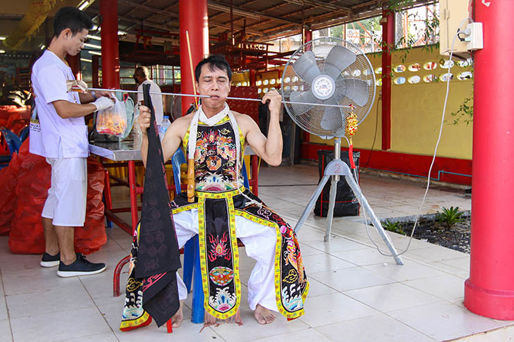 A spirit medium man with a metal spike piercing his cheek, cooling down next to a fan at Jor Soo Goong Naka Shrine, during Jay or Phuket Vegetarian Festival, also known as Thailand's self-mutilation festival; photo by Ivan Kralj.