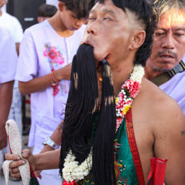 A possessed devotee with rolled-back eyes and pieces of fabric passing through his pierced cheeks and mouth, at Jor Soo Goong Naka Shrine, during Jay or Phuket Vegetarian Festival, also known as Thailand's self-mutilation festival; photo by Ivan Kralj.