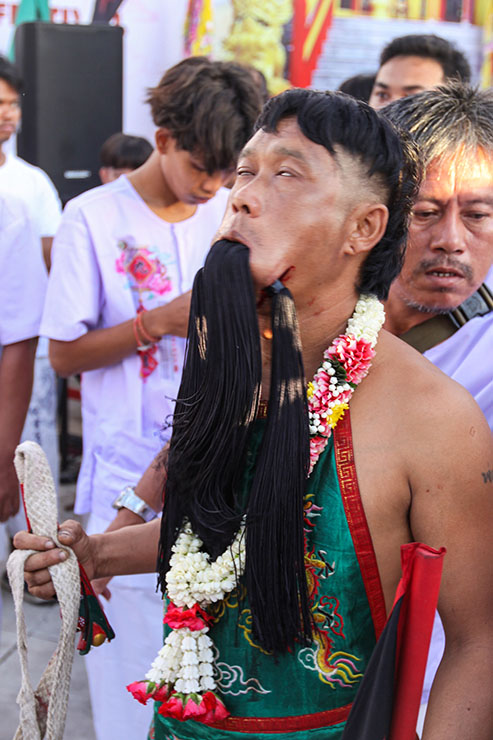 A possessed devotee with rolled-back eyes and pieces of fabric passing through his pierced cheeks and mouth, at Jor Soo Goong Naka Shrine, during Jay or Phuket Vegetarian Festival, also known as Thailand's self-mutilation festival; photo by Ivan Kralj.