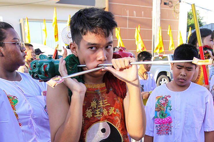 A young man holding two metal rods piercing his cheeks, at Jor Soo Goong Naka Shrine, during Jay or Phuket Vegetarian Festival, also known as Thailand's self-mutilation festival; photo by Ivan Kralj.