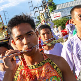 A close-up of a man with pierced cheeks, walking in a street procession through Phuket during Jay or Vegetarian Festival, also known as Thailand's self-mutilation festival; photo by Ivan Kralj.