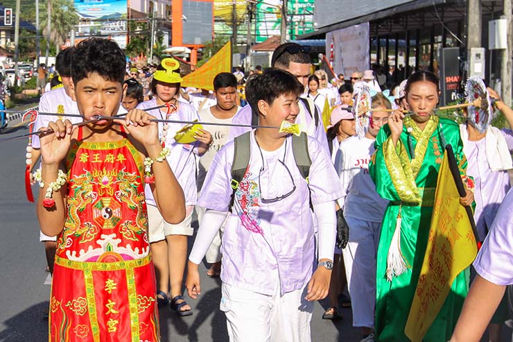 A young boy and a woman, both with pierced cheeks, walking in a street procession through Phuket during Jay or Vegetarian Festival, also known as Thailand's self-mutilation festival; photo by Ivan Kralj.