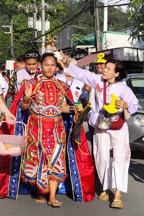A woman wiping off the sweat from a forehead of a ma song, a spirit medium woman possessed by one of the Nine Emperor Gods, walking in a street procession through Phuket during Jay or Vegetarian Festival, also known as Thailand's self-mutilation festival; photo by Ivan Kralj.