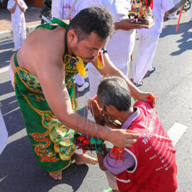 Ma song, a man with pierced cheeks, blessing an older man kneeling in the street during a procession of Jay or Vegetarian Festival, also known as Thailand's self-mutilation festival; photo by Ivan Kralj.