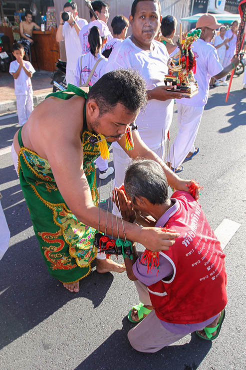 Ma song, a man with pierced cheeks, blessing an older man kneeling in the street during a procession of Jay or Vegetarian Festival, also known as Thailand's self-mutilation festival; photo by Ivan Kralj.
