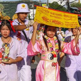 A woman with pierced cheeks hiding from sun behind a flag, while walking in a street procession through Phuket during Jay or Vegetarian Festival, also known as Thailand's self-mutilation festival; photo by Ivan Kralj.