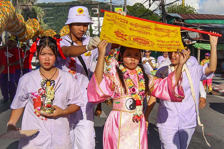 A woman with pierced cheeks hiding from sun behind a flag, while walking in a street procession through Phuket during Jay or Vegetarian Festival, also known as Thailand's self-mutilation festival; photo by Ivan Kralj.