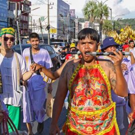 A young man with a knife piercing his cheek, walking in a street procession through Phuket during Jay or Vegetarian Festival, also known as Thailand's self-mutilation festival; photo by Ivan Kralj.