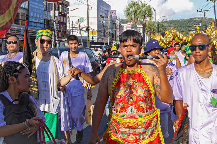 A young man with a knife piercing his cheek, walking in a street procession through Phuket during Jay or Vegetarian Festival, also known as Thailand's self-mutilation festival; photo by Ivan Kralj.
