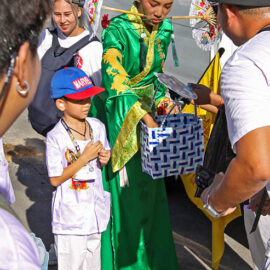 A woman with sun umbrellas piercing her cheeks giving out candies to children during Jay or Phuket Vegetarian Festival, also known as Thailand's self-mutilation festival; photo by Ivan Kralj.