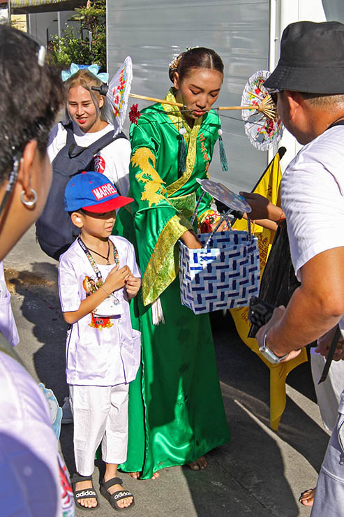 A woman with sun umbrellas piercing her cheeks giving out candies to children during Jay or Phuket Vegetarian Festival, also known as Thailand's self-mutilation festival; photo by Ivan Kralj.