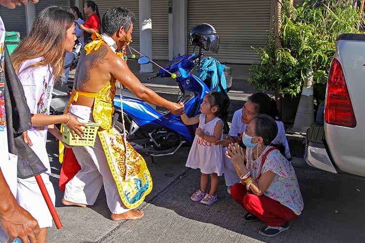 A man with pierced cheeks handing out candies to children during Jay or Phuket Vegetarian Festival, also known as Thailand's self-mutilation festival; photo by Ivan Kralj.