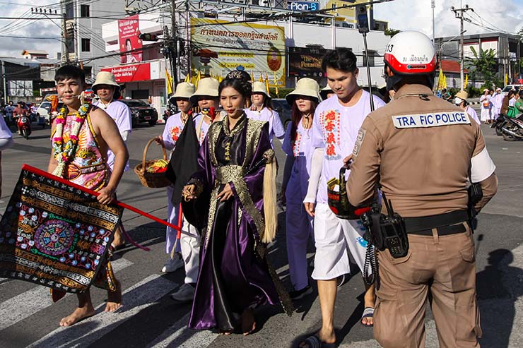 A traffic policeman filming a man and a woman with pierced cheeks while they walk in the street procession of Jay or Phuket Vegetarian Festival, also known as Thailand's self-mutilation festival; photo by Ivan Kralj.