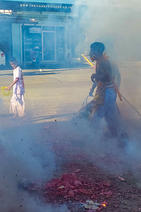 A ma song (spirit medium) with pierced cheeks, walking through the smoke created by exploding firecrackers in the streets of Phuket, during Jay or Phuket Vegetarian Festival; photo by Ivan Kralj.