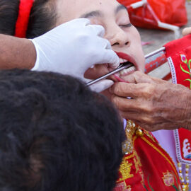 A metal rod piercing a cheek of a woman, a ma song spirit medium at Jor Soo Goong Naka Shrine, during Jay or Phuket Vegetarian Festival, also known as Thailand's self-mutilation festival; photo by Ivan Kralj.
