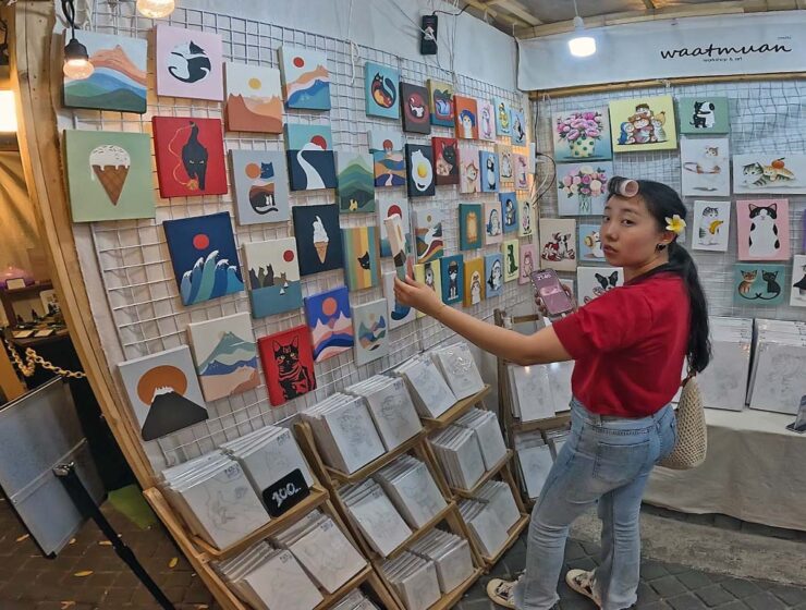 Young woman with a curler in her hair observing a painting being sold at the White Market, one of Nimman night markets in Chiang Mai, Thailand; photo by Ivan Kralj.