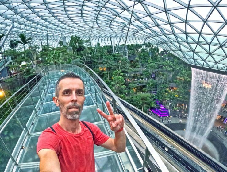 Travel blogger Ivan Kralj standing on Mastercard Canopy Bridge with Rain Vortex in the background, the world's largest indoor waterfall in a stunning Jewel complex of Singapore Changi Airport; photo by Ivan Kralj.
