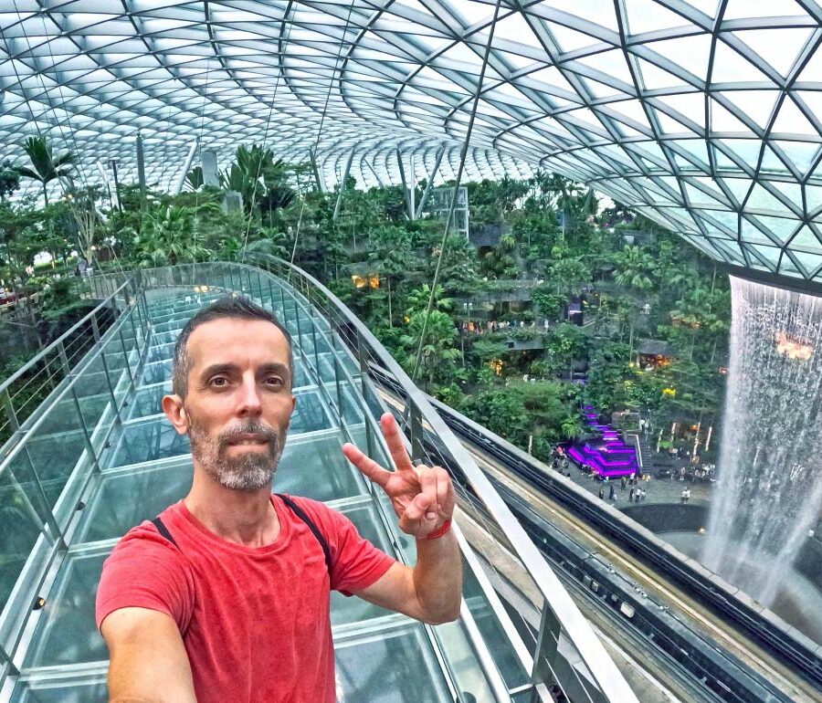 Travel blogger Ivan Kralj standing on Mastercard Canopy Bridge with Rain Vortex in the background, the world's largest indoor waterfall in a stunning Jewel complex of Singapore Changi Airport; photo by Ivan Kralj.